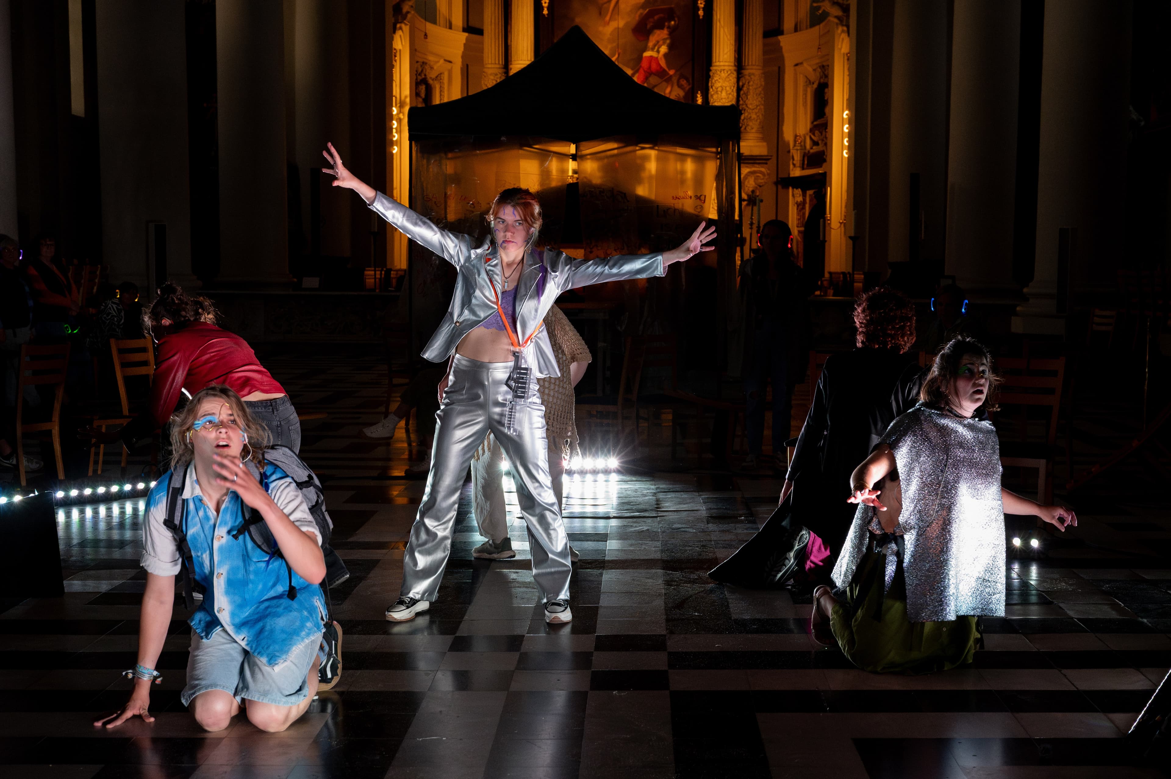 Een speler in een zilveren pak met gespreide armen in een kerk, anderen knielen rond haar
